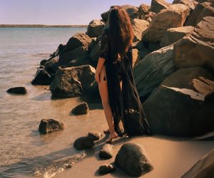 Woman in black standing among sunlit rocks on the Constanța shoreline