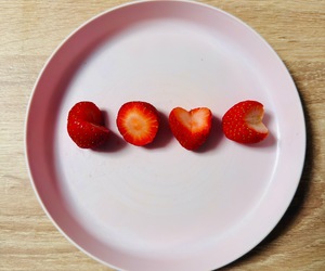 Four bitten and cut strawberries on a pale pink plate, the third shaped like a heart